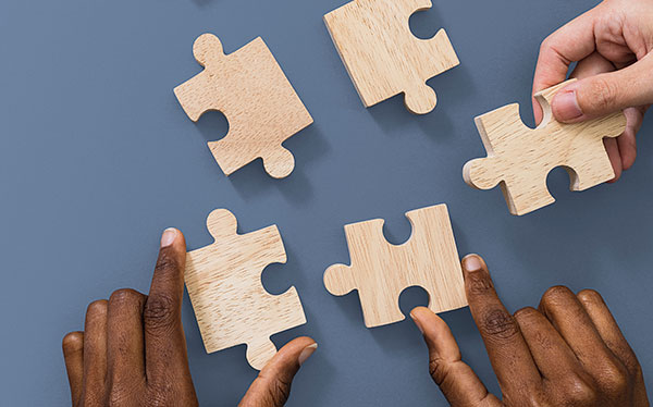 Foto de três mãos segurando peças de quebra-cabeça de madeira